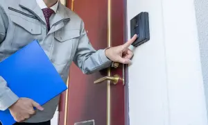 Mężczyzna w szarym stroju roboczym z teczką dzwoni domofonem. Może to być kontrola ZUS na L4.