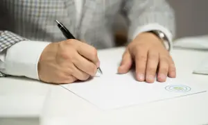 Mężczyzna w eleganckim garniturze dokonuje korekty świadectwa pracy, pisząc długopisem na dokumencie z pieczęcią.