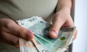 Dłonie trzymają stos banknotów 100 zł. To może być pomoc de minimis dla przedsiębiorcy.