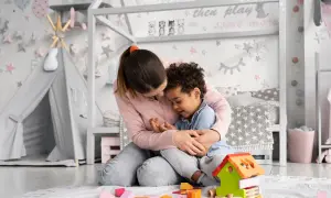 Ciepła opieka na dziecko w pokoju pełnym zabawek. Kobieta tuli chłopca, otoczeni kolorowymi klockami i namiotem tipi.