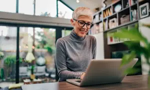 Uśmiechnięta kobieta z krótkimi blond włosami pracuje na laptopie. Może sprawdza swój dodatek do wynagrodzenia.