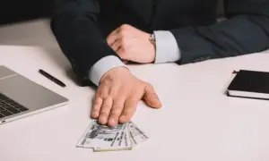 Mężczyzna w garniturze podaje pieniądze, być może jako dodatek stażowy. Obok laptop i notatnik.