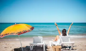 Kobieta cieszy się słońcem na plaży, zastanawiając się, ile dni urlopu jeszcze jej zostało. Obok leżaki i parasol.