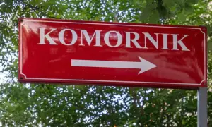 Czerwony znak drogowy z napisem "KOMORNIK" i białą strzałką w prawo. Może symbolizować drogę do komornika, gdy umowa zlecenie jest zagrożona.