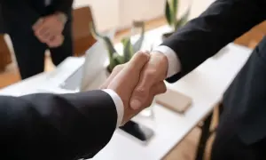 Dwaj prawnicy ściskają sobie dłonie, symbolizując udane porozumienie na rynku prawniczym.