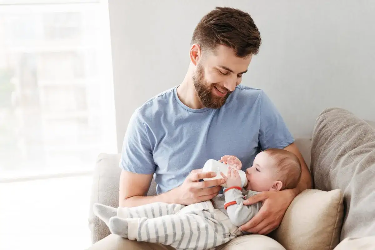 Szczęśliwy ojciec karmi dziecko butelką, ciesząc się urlopem rodzicielskim dla ojca.