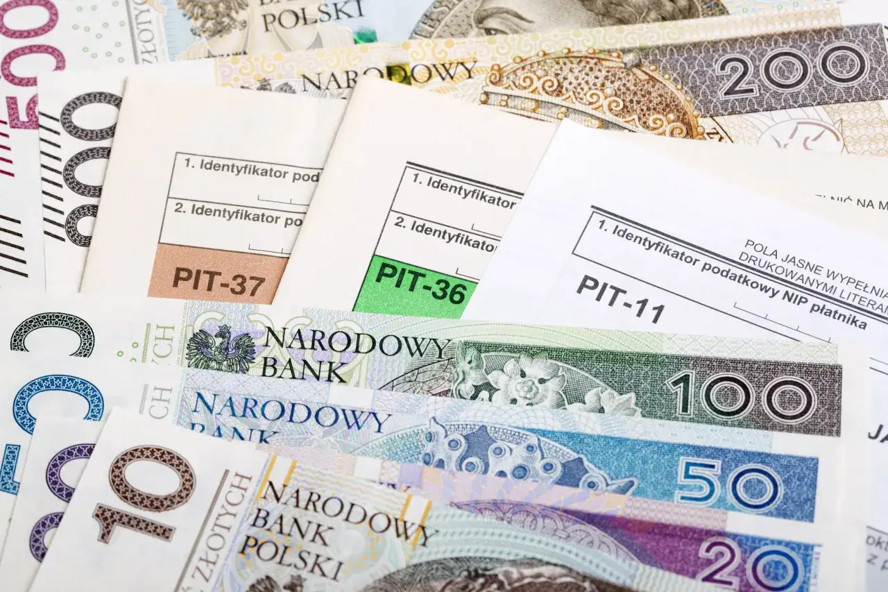 Formularze PIT-37, PIT-36, PIT-11 leżą na stosie polskich banknotów. Czas rozliczyć podatki i sprawdzić, jaka jest kwota wolna od podatku.