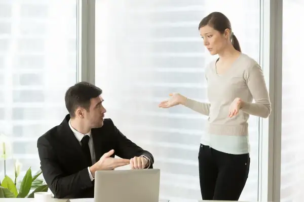 Mężczyzna w garniturze pokazuje na zegarek, kobieta gestykuluje. Dyskutują o wezwaniu do sądu a praca.