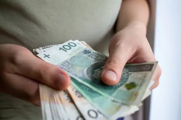 Dłonie trzymają stos banknotów 100 zł. To może być pomoc de minimis dla przedsiębiorcy.